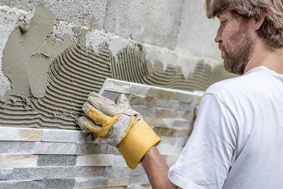 Person verlegt Natursteinwand mit Kelle
